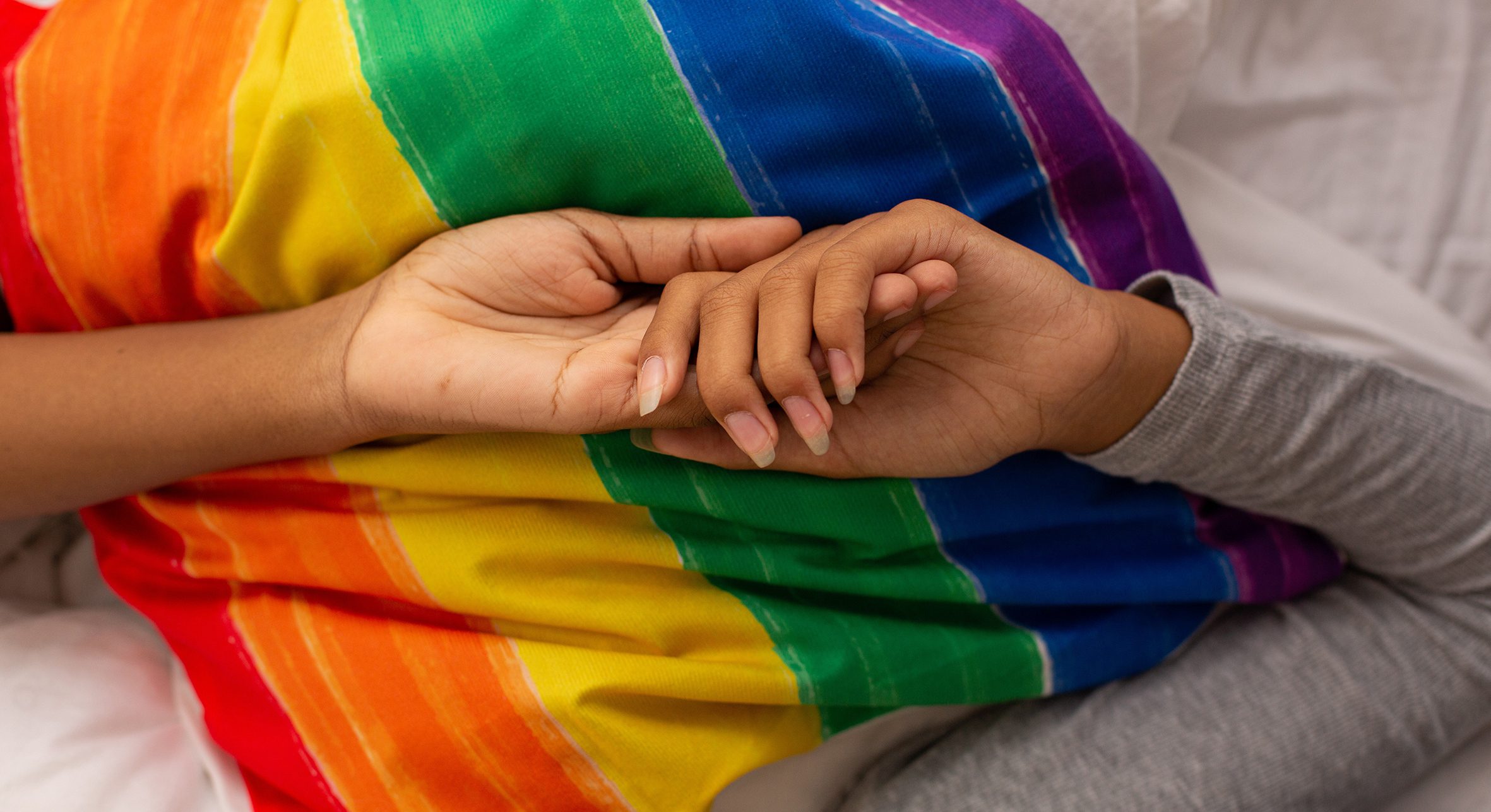 Two females holding hands on rainbow flag.